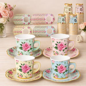 May include: A set of four paper cups and matching saucers in pastel mint, pink, yellow, and blue, each featuring a pink rose pattern and white polka dots. The collection includes stacks of additional paper cups and circular floral paper coasters.