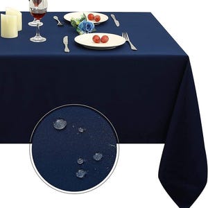 May include: A solid navy blue rectangular tablecloth covering a table set with white plates, silver forks, silver knives, wine glasses, and candles. A circular inset shows a close-up of the fabric texture with several water droplets on it.