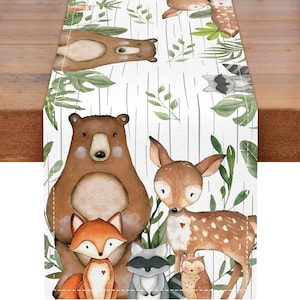May include: A white table runner featuring a repeating pattern of woodland animals including brown bears, deer, foxes, raccoons, and owls, interspersed with green leaves and thin vertical gray lines on a textured fabric surface.