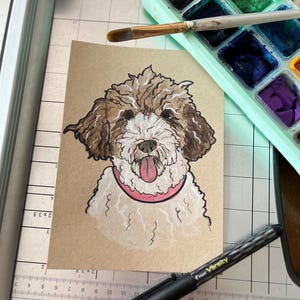 May include: A hand-drawn illustration of a curly-haired dog with brown and white fur, wearing a pink collar, depicted on a rectangular piece of tan paper. The dog has a pink tongue visible and is rendered with black ink outlines and white highlights.