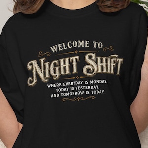 以下が含まれることがあります： 黒いTシャツで、「WELCOME TO NIGHT SHIFT」という大きなかすれたオフホワイトのセリフ体テキストと、その下に「WHERE EVERYDAY IS MONDAY, TODAY IS YESTERDAY, AND TOMORROW IS TODAY」という小さくシンプルなサンセリフ体のテキストがプリントされています。
