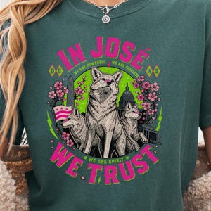 May include: Teal green t-shirt with a graphic featuring three coyotes, cherry blossoms, and the text "IN JOSE WE TRUST." The design includes the text "WE ARE POWERFUL" and "WE ARE FEARLESS."