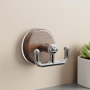 May include: A wall-mounted double hook with a wood-grain finish and a polished chrome hook. The round wooden base is attached to the wall. The hook has a U-shaped design with two rounded ends.