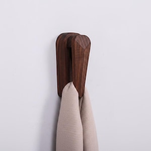 May include: A dark brown wooden wall hook with a curved design. A beige scarf hangs from the hook. The hook is mounted on a white wall. The hook is made of solid wood and has a smooth finish.