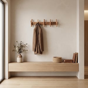 May include: A minimalist entryway scene featuring a wooden coat rack with pegs, a brown coat, and a floating wooden bench. A vase with greenery, a woven basket, and books add to the decor. The room has a neutral color palette with natural light.