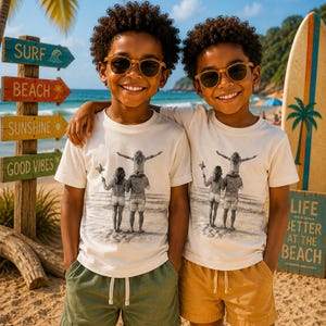 Peut inclure: Deux enfants portant des t-shirts crème assortis avec un croquis en noir et blanc d'une famille sur la plage. Un enfant porte un short vert olive, l'autre un short jaune moutarde. Tous deux portent des lunettes à monture marron sur le sable.