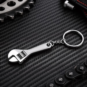 May include: A silver-coloured metal keyring shaped like a miniature adjustable spanner. The keyring features a functional-looking worm gear mechanism on the head of the spanner and is attached to a standard circular split ring by a short metal chain.