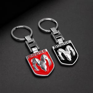 Peut inclure: Deux porte-clés en métal arborant le logo du bélier Dodge. L'un possède un fond en émail rouge et l'autre un fond en émail noir. Les deux présentent le mot DODGE en lettres argentées au-dessus de l'emblème de tête de bélier et un anneau.