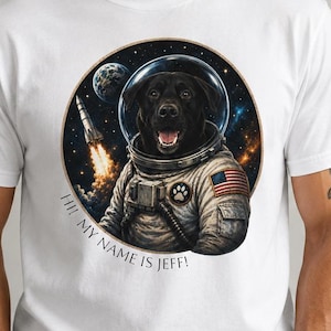 May include: White t-shirt featuring a black Labrador in an astronaut suit, set against a space backdrop with a rocket. The text "HI! MY NAME IS JEFF!" is printed on the shirt. The image is a digital illustration.