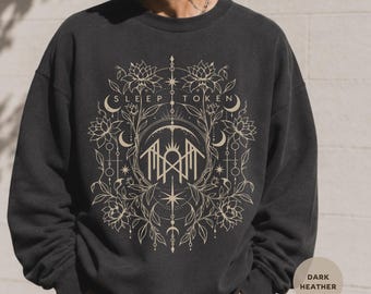 Puede incluir: Una sudadera de cuello redondo en gris jaspeado oscuro con un estampado gráfico en beige del texto Sleep Token rodeado de intrincados dibujos de líneas de flores de loto, lunas crecientes, estrellas y símbolos geométricos en el pecho.