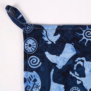 May include: Blue cotton pot holder with a white design of stylized birds and geometric shapes. The pot holder has a loop handle.