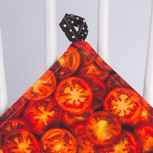 May include: A square, quilted pot holder with a vibrant tomato slice pattern. The fabric features a repeating design of red and orange tomato slices. It has a black and white polka dot loop for hanging.