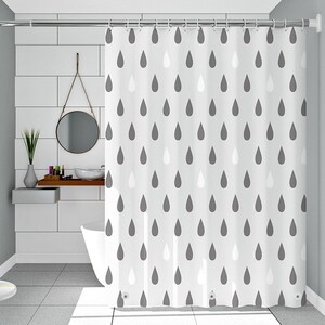 May include: A white shower curtain featuring a repeating pattern of dark gray and light gray teardrop shapes. The curtain is suspended from a silver metal rod with circular rings and includes reinforced grommets along the bottom edge for stability.