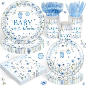 May include: A party supply set featuring plates, cups, and napkins decorated with blue floral patterns and baby items hanging on a clothesline. The text "BABY in bloom" is printed on the plates and cups, accompanied by blue plastic forks and knives.