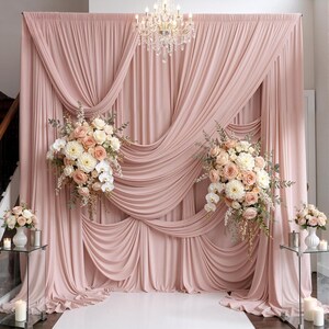 May include: A dusty rose fabric backdrop featuring elegant drapes and swags, adorned with two large floral arrangements of white and peach roses, dahlias, and orchids, complemented by two smaller matching bouquets on glass pedestals with candles.