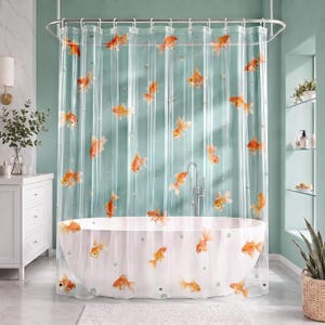 May include: A clear plastic shower curtain featuring a repeating pattern of orange goldfish and small bubbles. The curtain is suspended from a silver metal rod with circular rings and hangs in front of a white oval bathtub in a bathroom setting.