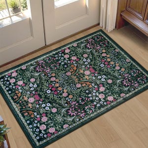 May include: A rectangular area rug featuring a dark green background with a dense, symmetrical pattern of pink, white, and orange flowers, green leaves, and winding vines. The rug has a thin, dark green border framing the intricate floral design.