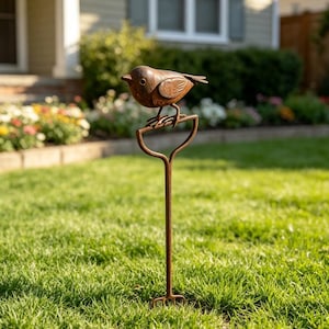 Könnte beinhalten: Ein rostfarbener Metall-Gartenstecker mit einem kleinen Vogel, der auf einem griffartigen Rahmen sitzt. Der Vogel hat einen abgerundeten Körper und strukturierte Flügel, während der Stecker aus einem langen, dünnen Stab mit einer kleinen Basis besteht.