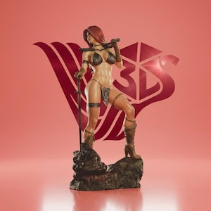 May include: A bronze figurine of a warrior woman with red hair, wearing a chainmail bikini and boots, holding a sword. The figure stands on a rocky base against a pink background with a stylized logo.