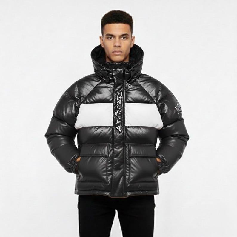 May include: Black puffer jacket with a white horizontal stripe across the chest. The jacket has a high collar, two front pockets, and the brand name "Avirex" in white lettering down the center. The jacket is worn by a person.