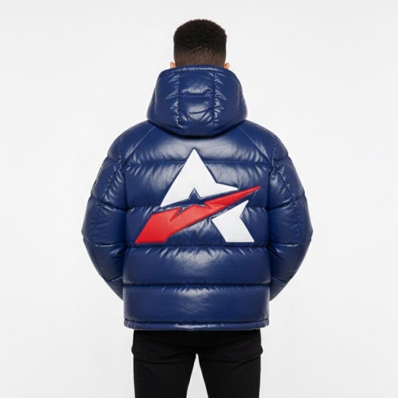 May include: A navy blue puffer jacket with a large white and red logo on the back. The jacket has a hood and a shiny, quilted texture. The person is wearing black trousers.