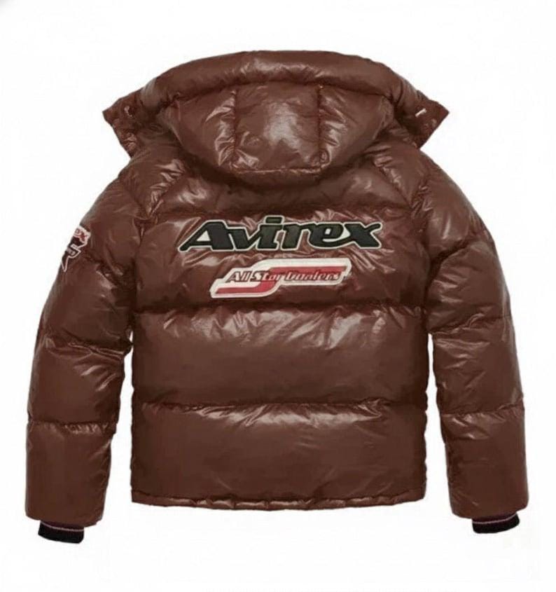 May include: Brown puffer jacket with a hood. The back of the jacket features the brand name "Avirex" in white and black lettering, with "All Star Dealers" below. The jacket has a glossy finish and a patch on the left sleeve.
