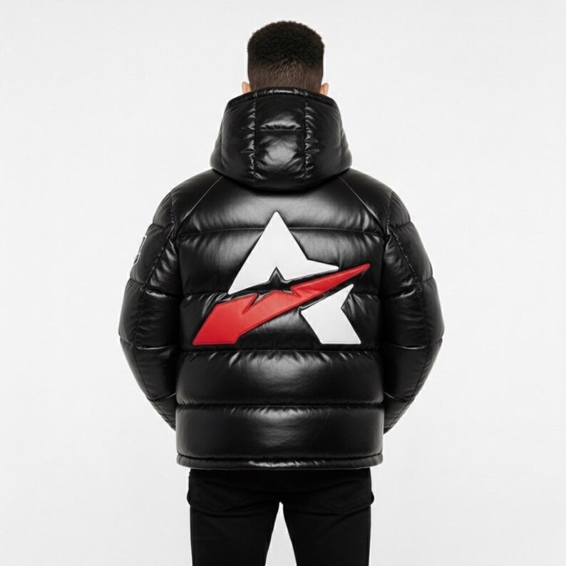 May include: Black puffer jacket featuring a large white and red logo on the back. The jacket has a hood and a shiny, quilted design. The model is wearing black trousers.