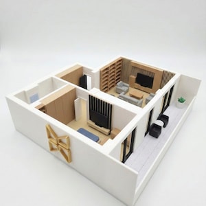 May include: A scale model of a multi-room apartment featuring white walls, light wood flooring, and detailed interior furnishings including sofas, televisions, shelving units, and a balcony with black chairs and a small potted plant.