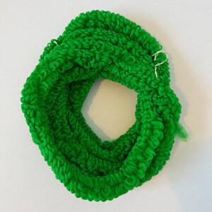 May include: Bright green, looped knit infinity scarf. The scarf is circular, with a thick, textured appearance. The yarn is a vibrant, solid green color. The scarf is shown on a white background.