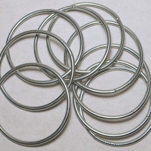 May include: A set of ten silver metal rings, stacked and overlapping, creating a circular pattern.