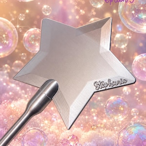 May include: A silver-toned metal star-shaped wand featuring a smooth, brushed finish and a long, slender handle. The name Stephanie is engraved in a cursive script on the lower right point of the star. The object is set against a background of bubbles.