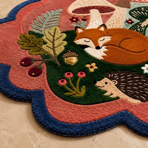 May include: A scalloped-edge area rug featuring a forest scene with a sleeping orange fox, a small hedgehog, mushrooms, ferns, and an acorn. The rug has a deep blue border, a dusty rose background, and dark green accents with floral details.