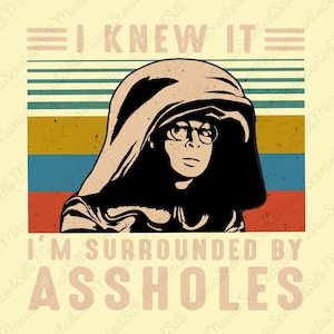 May include: A graphic print featuring a stylized illustration of a person wearing a hooded cloak and round glasses. The text I KNEW IT appears above the figure, and I'M SURROUNDED BY ASSHOLES appears below, set against a background of horizontal stripes.