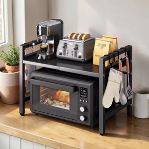 Puede incluir: Estantería de cocina de metal negro con cafetera, tostadora con pan y un horno pequeño. El horno muestra un reloj digital y la temperatura. Ganchos colgantes sostienen guantes de cocina y utensilios. Dos bolsas de café en la estantería.