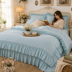May include: A light blue bedding set featuring a ruffled duvet cover and matching pillow shams. The set includes a textured fabric finish with layered ruffles along the edges, creating a soft appearance on a bed frame with a headboard.