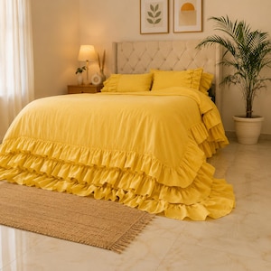 Può includere: Un copriletto giallo brillante caratterizzato da tre strati di balze a cascata lungo i bordi. Il set di biancheria da letto include federe gialle abbinate posizionate contro una testiera trapuntata, creando un aspetto monocromatico uniforme.