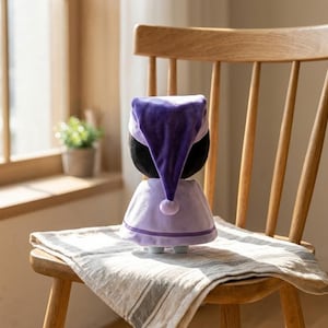 May include: A plush doll wearing a purple nightcap and a matching dress, trimmed with light purple and a small pom-pom. The doll is on a wooden chair with a striped cloth.
