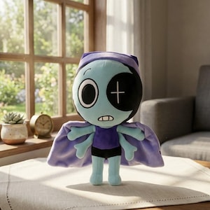 May include: A soft toy doll with a teal face, one large eye, and a black eye with a white cross. It wears a purple outfit, black shorts, and a lilac cape. The doll is on a table in front of a window.