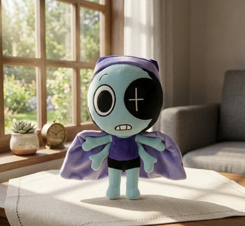 May include: A soft toy doll with a teal face, one large eye, and a black eye with a white cross. It wears a purple outfit, black shorts, and a lilac cape. The doll is on a table in front of a window.