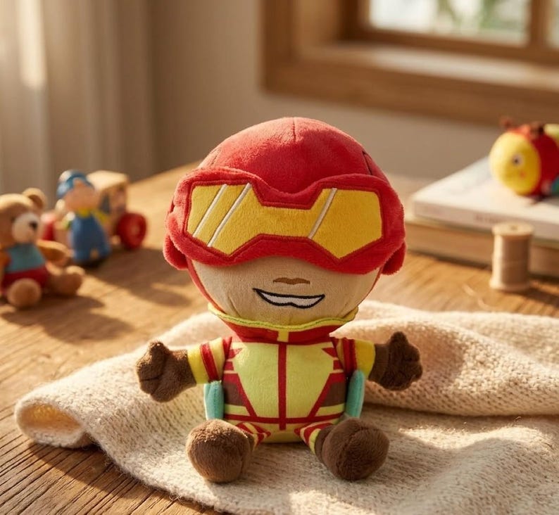 May include: A plush superhero doll with a red helmet and yellow visor. The doll has a yellow and red suit with brown gloves and shoes. Other plush toys are in the background.