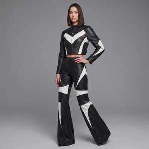 May include: A black and white leather two-piece set consisting of a cropped long-sleeve jacket with a high neck and a front zipper, paired with matching high-waisted flared trousers. Both pieces feature bold, geometric white leather paneling.