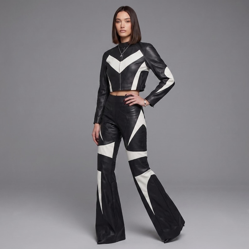 May include: A black and white leather two-piece set consisting of a cropped long-sleeve jacket with a high neck and a front zipper, paired with matching high-waisted flared trousers. Both pieces feature bold, geometric white leather paneling.