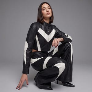 May include: A black and white leather jacket and matching wide-leg leather trousers. The jacket features a high collar and a chevron-patterned white panel across the chest. The trousers have coordinating white curved panels along the legs.