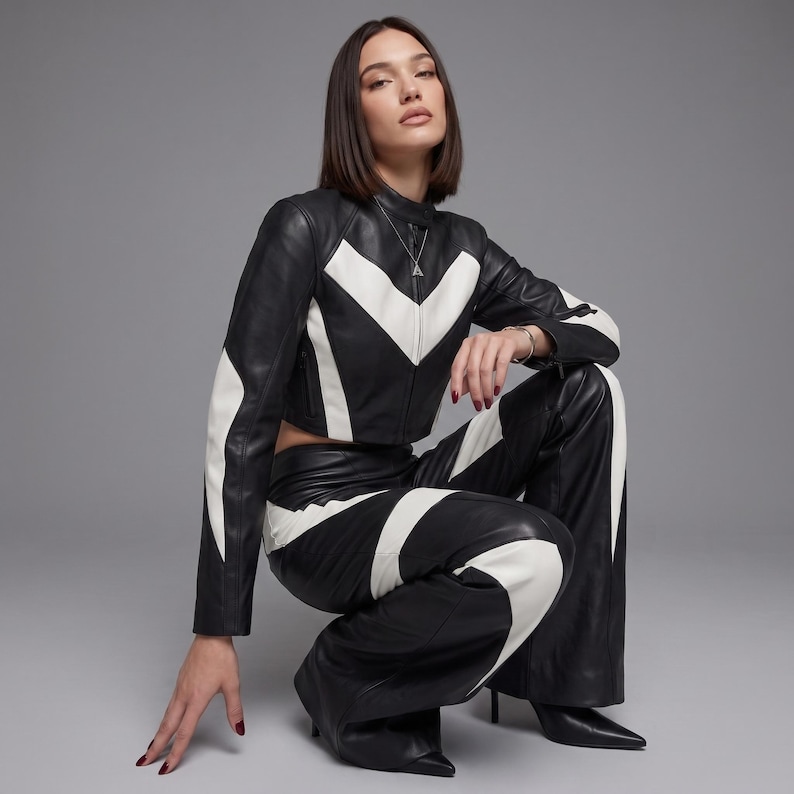 May include: A black and white leather jacket and matching wide-leg leather trousers. The jacket features a high collar and a chevron-patterned white panel across the chest. The trousers have coordinating white curved panels along the legs.
