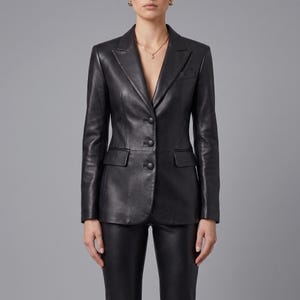 K&ouml;nnte beinhalten: Ein schwarzer Lederblazer mit steigendem Revers, langen &Auml;rmeln und einer Knopfleiste mit drei Kn&ouml;pfen. Die Jacke verf&uuml;gt &uuml;ber zwei Seitentaschen mit Klappen und strukturierte Schultern, was f&uuml;r eine taillierte Passform mit glatter Oberfl&auml;che sorgt.