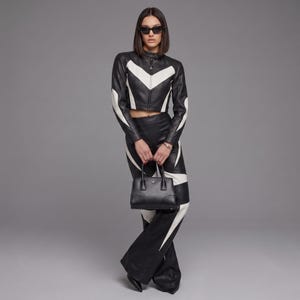 May include: A black and white leather cropped jacket and matching high-waisted flared trousers featuring chevron patterns. The outfit is paired with a structured black leather handbag with dual top handles and pointed-toe black leather boots.