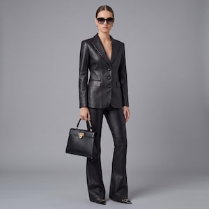 K&ouml;nnte beinhalten: Ein schwarzer Lederblazer mit drei Kn&ouml;pfen und dazu passender schwarzer Lederhose mit Schlag. Eine strukturierte schwarze Handtasche mit goldfarbenem Verschluss wird in der Hand gehalten. Eine dunkle Sonnenbrille vervollst&auml;ndigt das monochrome Outfit.