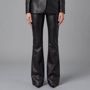 K&ouml;nnte beinhalten: Schwarze Lederhose mit einer eng anliegenden Passform an H&uuml;ften und Oberschenkeln, die sich ab dem Knie bis zum Saum ausstellt. Die Hose wird mit einer passenden schwarzen Lederjacke und spitzen Schuhen mit goldfarbenen Beschl&auml;gen kombiniert.