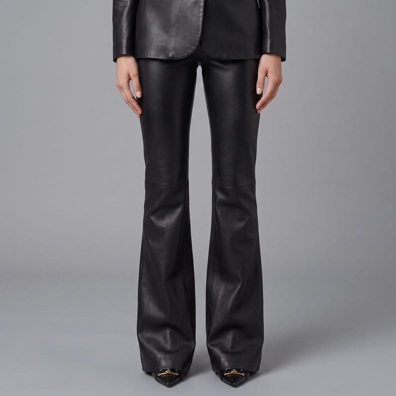 K&ouml;nnte beinhalten: Schwarze Lederhose mit einer eng anliegenden Passform an H&uuml;ften und Oberschenkeln, die sich ab dem Knie bis zum Saum ausstellt. Die Hose wird mit einer passenden schwarzen Lederjacke und spitzen Schuhen mit goldfarbenen Beschl&auml;gen kombiniert.