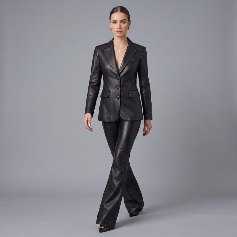 K&ouml;nnte beinhalten: Ein schwarzer Lederblazer mit steigendem Revers, drei Kn&ouml;pfen auf der Vorderseite und zwei Pattentaschen, kombiniert mit einer passenden, ausgestellten Lederhose in Schwarz. Das Set besteht aus glattem, dunklem Material mit leichtem Glanz.